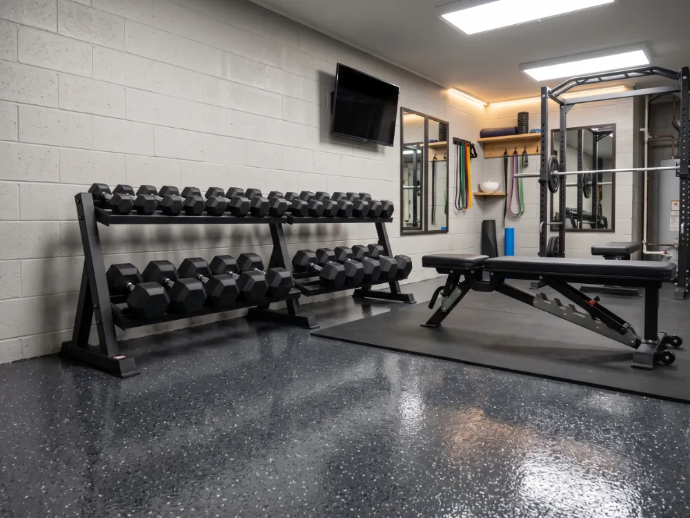 Basement home gym with a dark charcoal flake epoxy floor under bright LED lighting