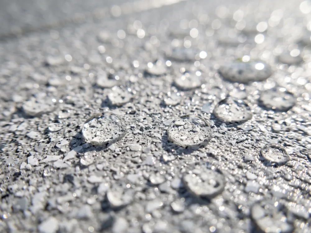 Light gray and white flake deck surface with beaded water droplets sparkling in sunlight