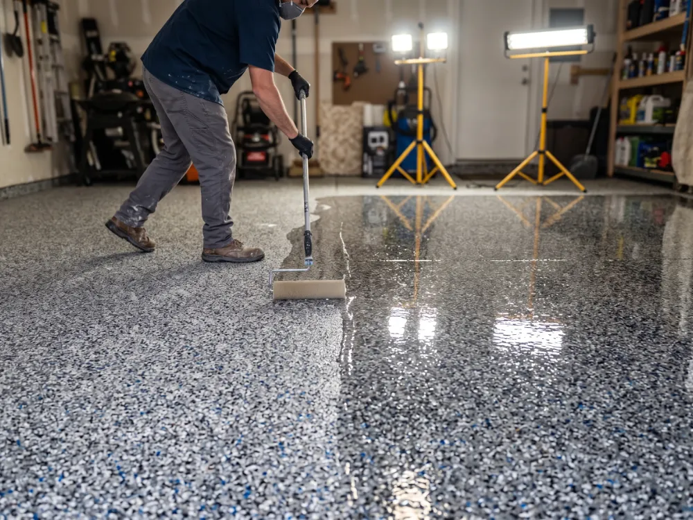 Installer rolling a glossy clear polyaspartic topcoat across a multicolor flake floor