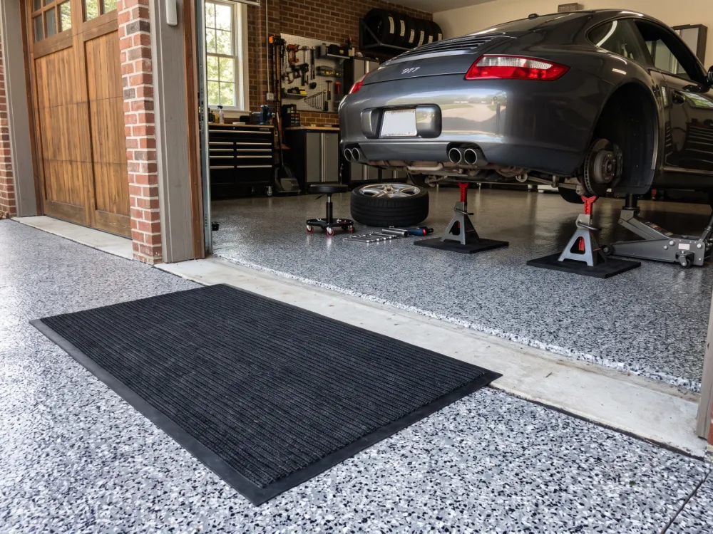 Walk-off mat at a garage entry and rubber pads under jack stands on a flake epoxy floor