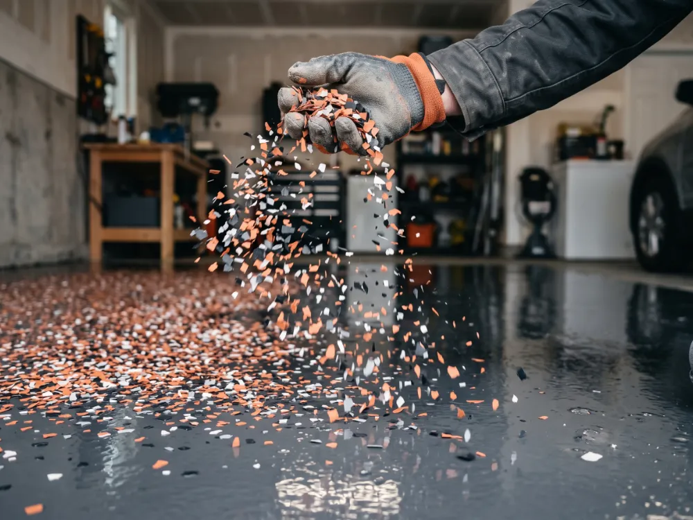 Gloved hand broadcasting terracotta and black vinyl flakes over a wet coated floor