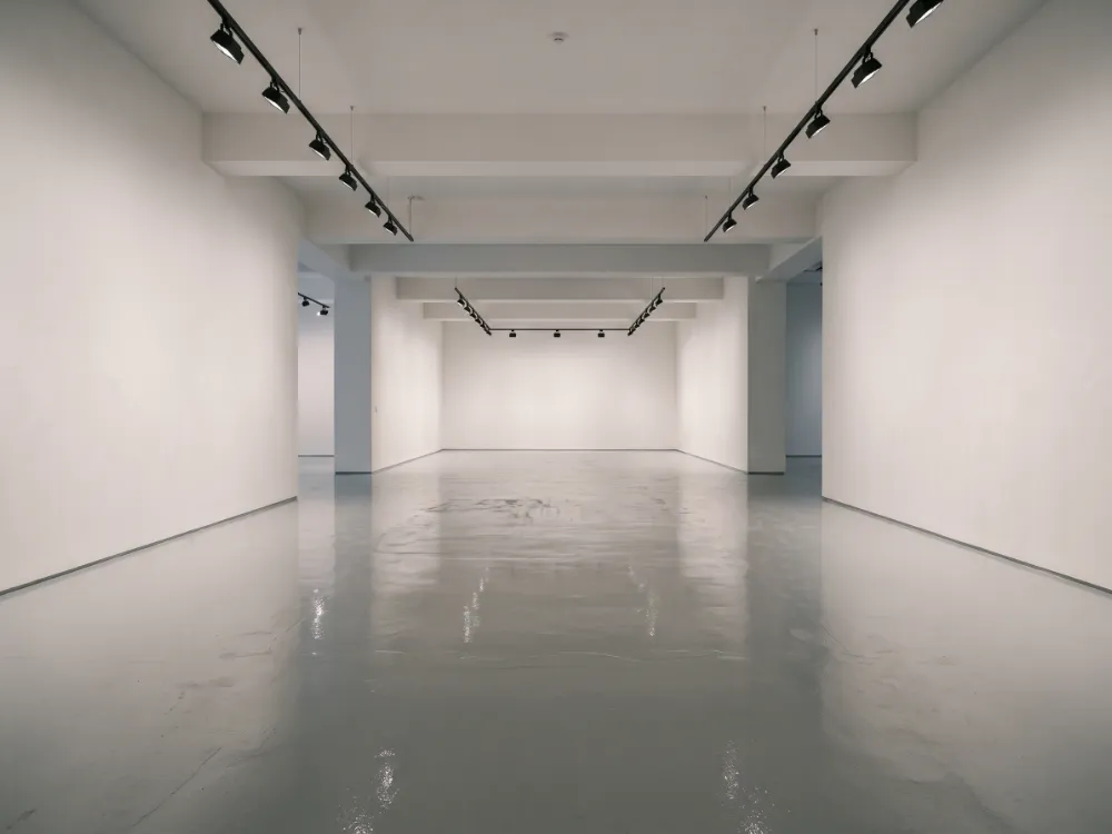 Empty gallery with bare walls and a freshly coated pale floor between exhibitions