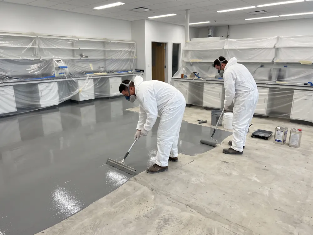 Technicians in coveralls coating a lab with benches sheeted