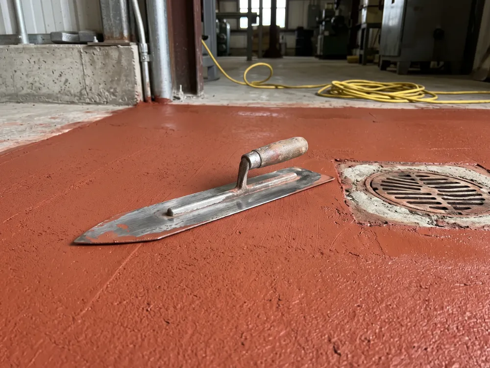 Steel trowel resting on freshly troweled brick-red urethane cement near a floor drain